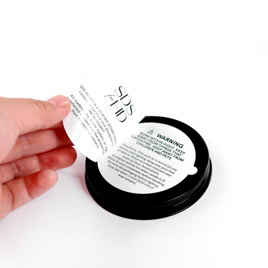 Booklet label on a black candle jar showing warning text