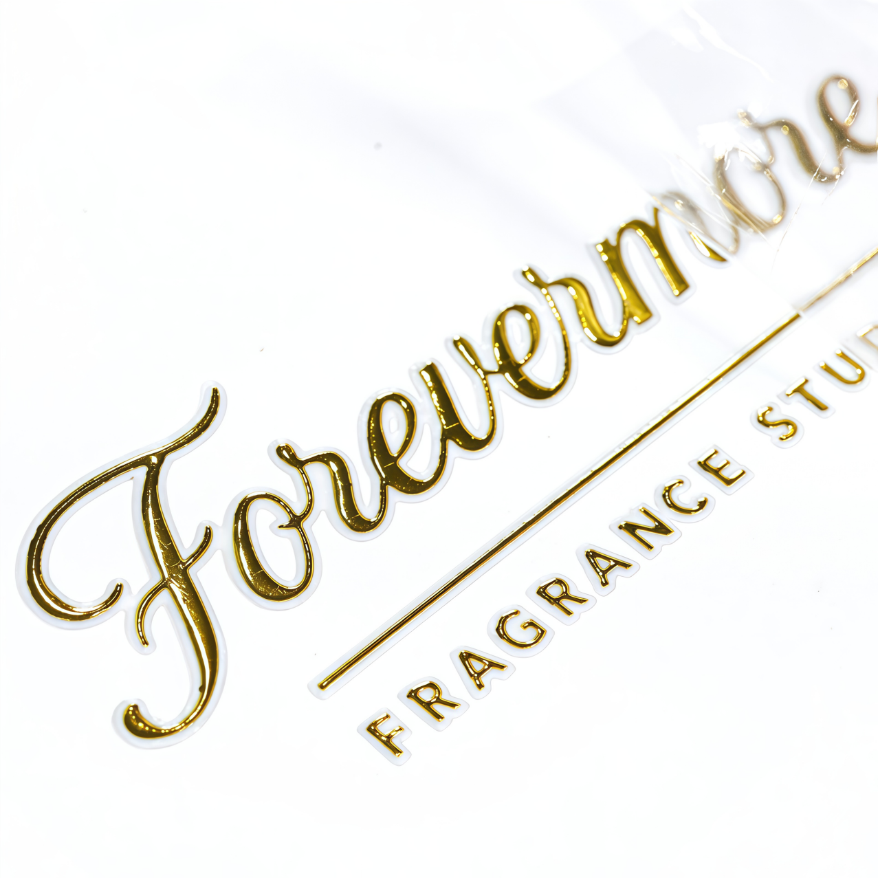 Gold foil transfer label on white background showing Forevermore Fragrance Studio script