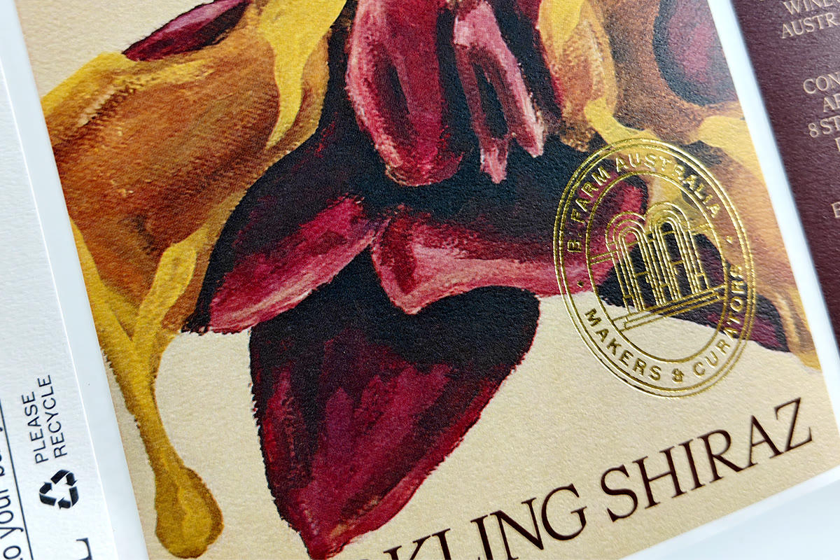 Close-up of a wine label on specialty paper: textured stock with gold foil emblem and hand-drawn illustration