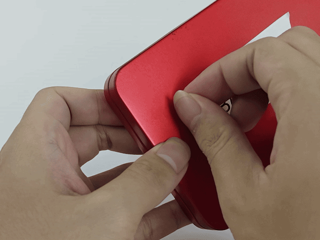Fragile label being torn from a red metal tin — the face stock fractures into pieces instead of peeling off whole